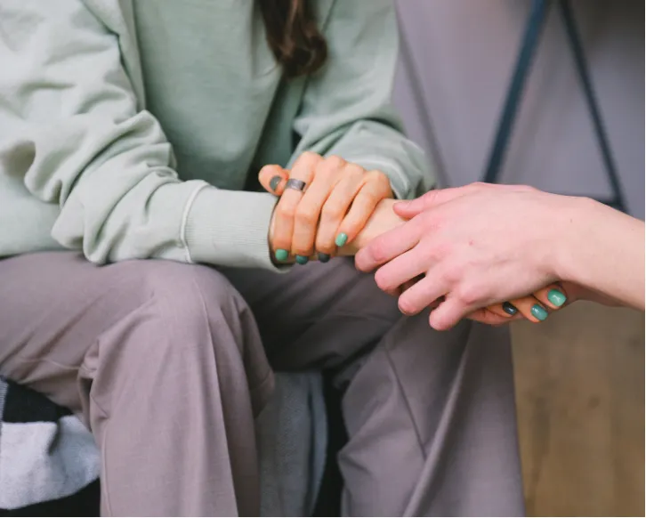 Two people sit close as one person gently holds the other's hand in a comforting gesture.